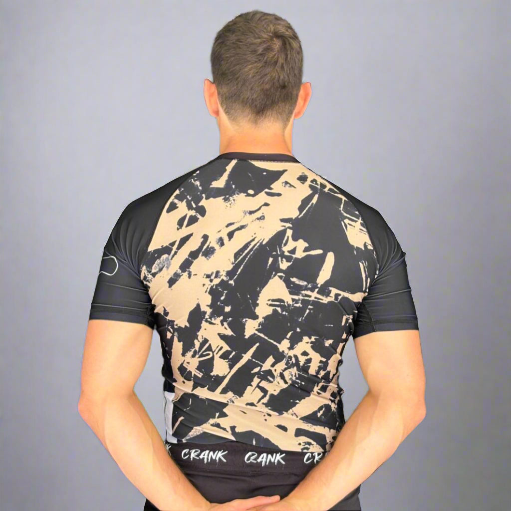 Person wearing a black and beige camouflage t-shirt against a gray wall.