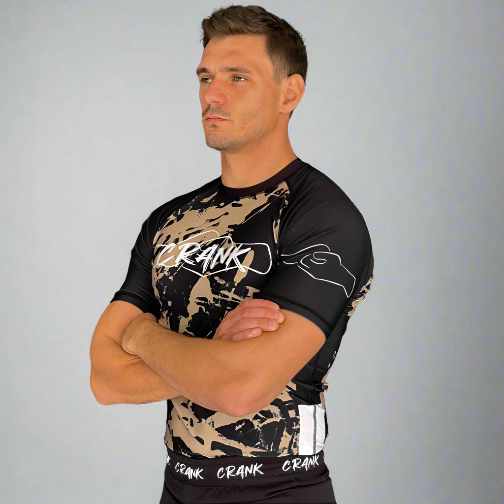 Man wearing a black and camouflage cycling jersey with 'Crank' branding against a gray wall.