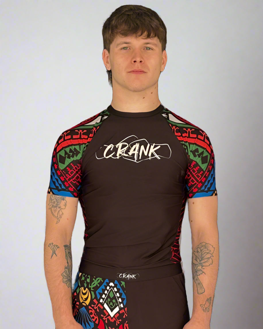 Person wearing a black and colorful athletic outfit with 'CRANK' branding against a gray wall.