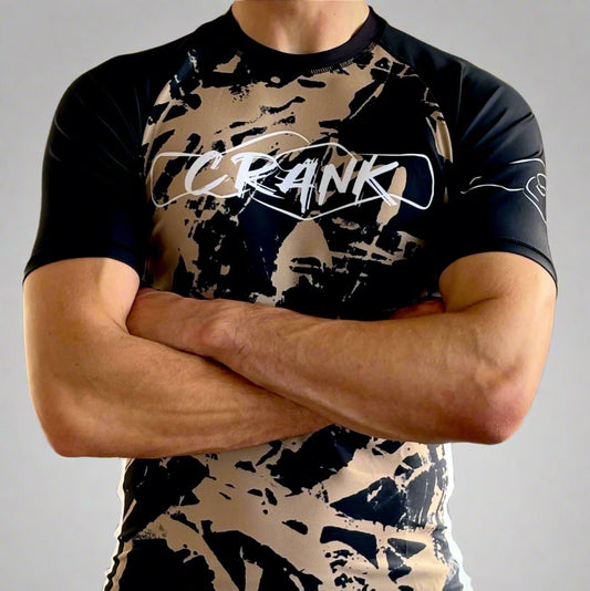 A person wearing a short sleeve rashguard with a camouflage pattern and the brand name 'Crank' across the chest.
