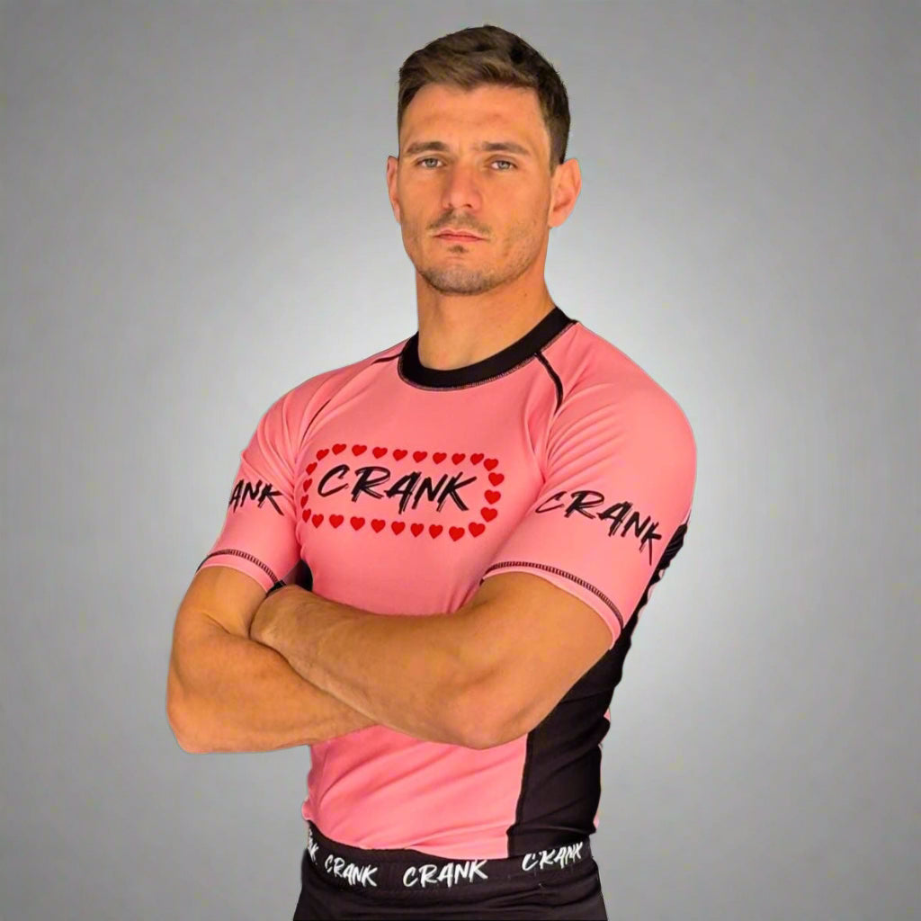 Man wearing a pink and black sports outfit with 'Crank' branding against a gray wall.