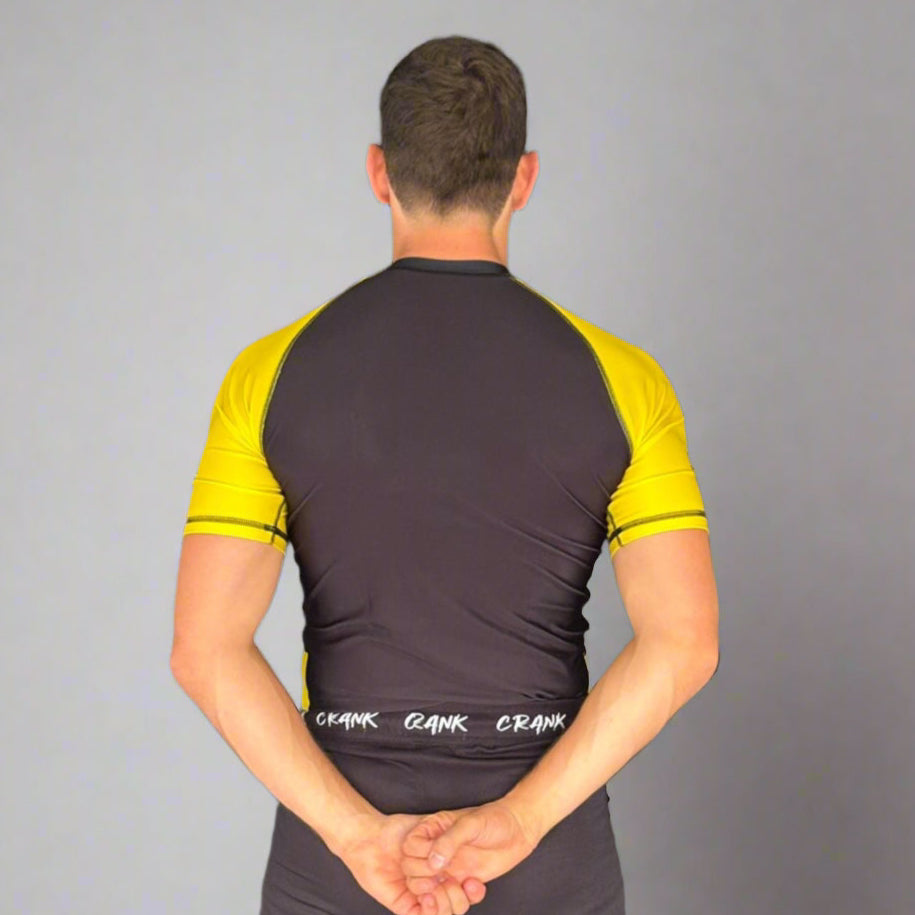 Person wearing a black and yellow athletic outfit standing against a gray wall.