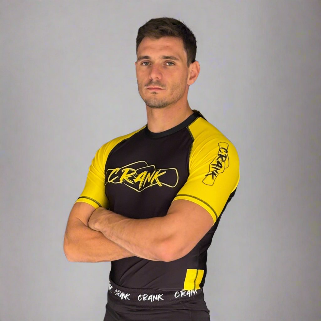 Man wearing a black and yellow athletic outfit with 'ZZ RAVK' branding against a gray wall.
