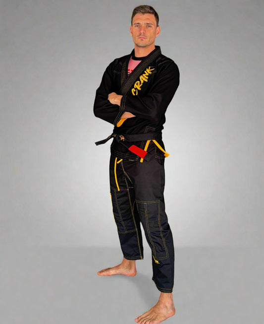 Man wearing a black martial arts uniform with visible branding against a gray wall.