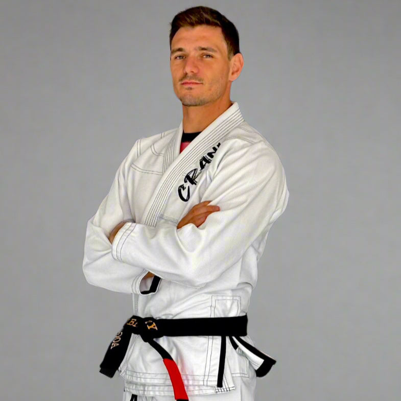 Person wearing a white martial arts uniform with a black belt against a dark wall.