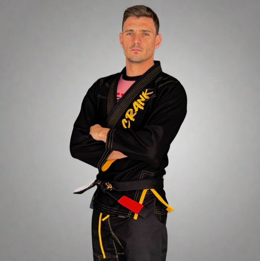 Man wearing a black martial arts uniform with visible branding against a gray wall.