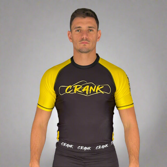Man wearing a black and yellow Rash Guard with 'Crank' branding against a gray background