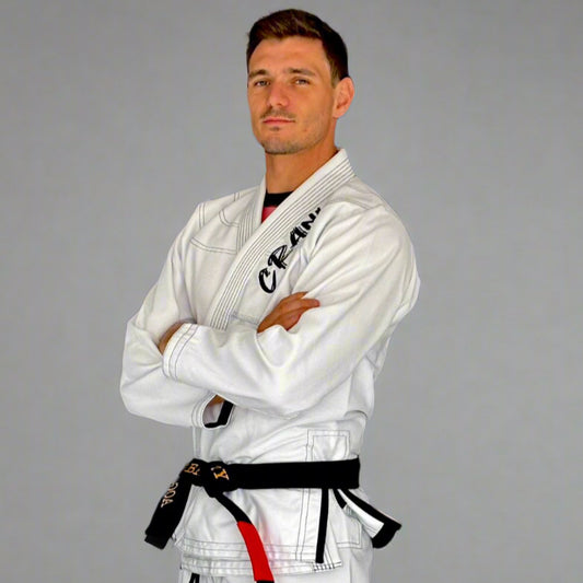 Person wearing a white martial arts uniform with a black belt against a dark wall.